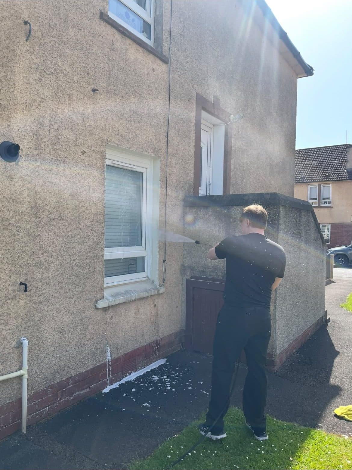 Cleaning roughcast render beside a garden